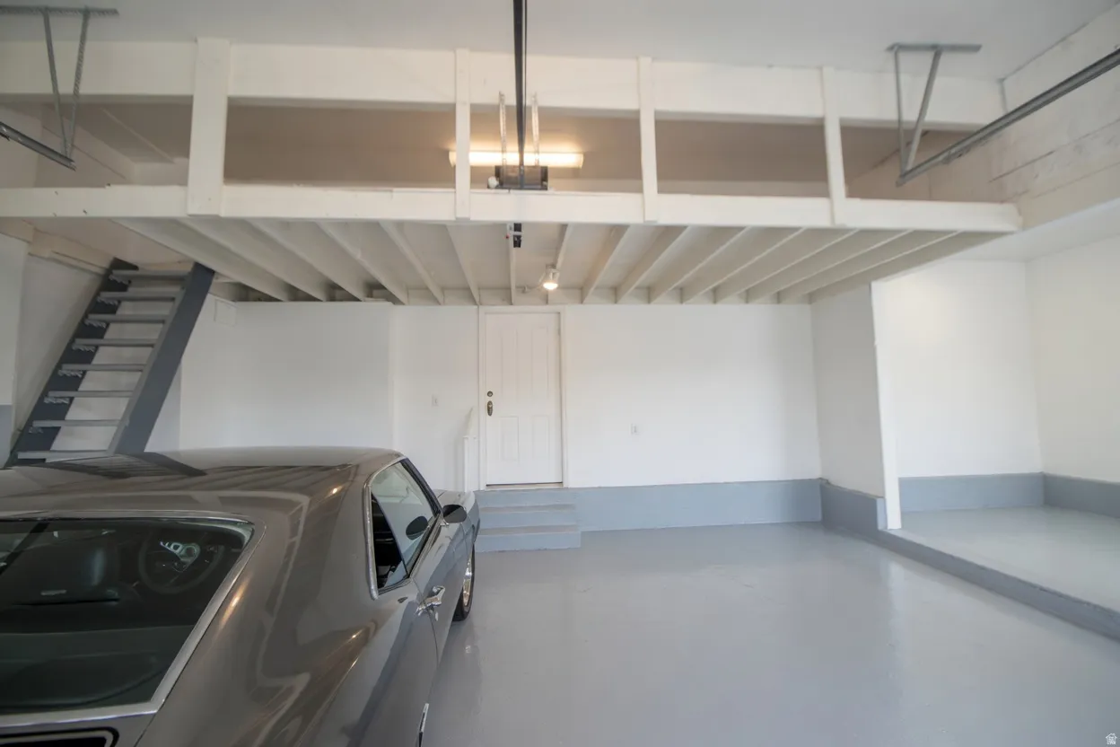 Spacious garage featuring a finished gray floor, white walls, and a substantial overhead storage loft with a gray metal staircase