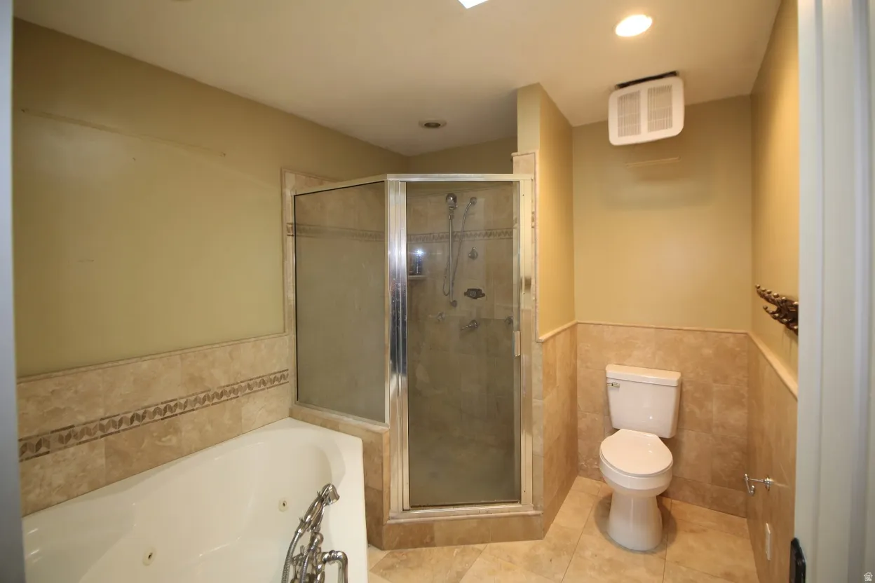 Master bathroom featuring a jetted tub, a glass-enclosed shower, a toilet, and light-toned tile flooring