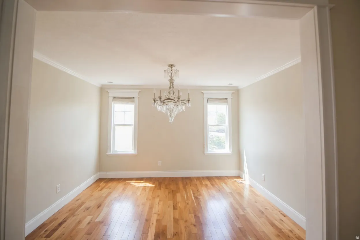 Spacious room featuring wood-finish flooring, a crystal chandelier, crown molding, and two windows with trim