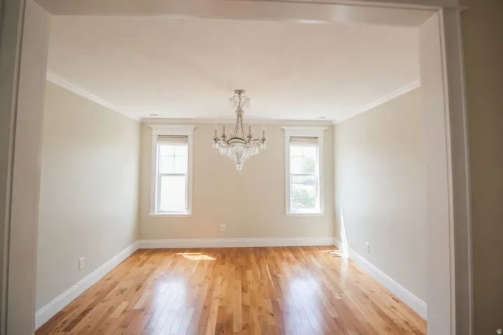 Spacious room featuring wood-finish flooring, a crystal chandelier, crown molding, and two windows with trim