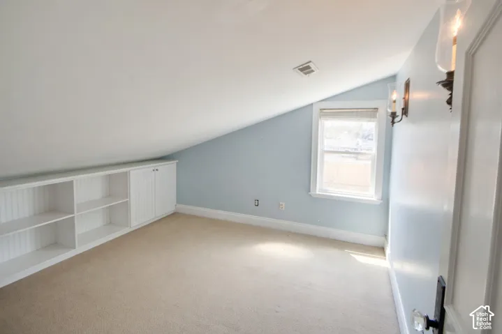 Bedroom 4 or nursery sloped ceiling room featuring a built-in white storage unit with shelving and cabinetry, a single window, and two wall sconces