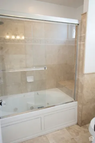 Tub and shower combination with sliding glass doors, surrounded by large format tile with a decorative accent band, and featuring a built-in shower bench, toilet.