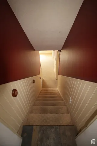 Carpeted staircase featuring beadboard wainscoting and wall sconces, descending to a slate tile landing