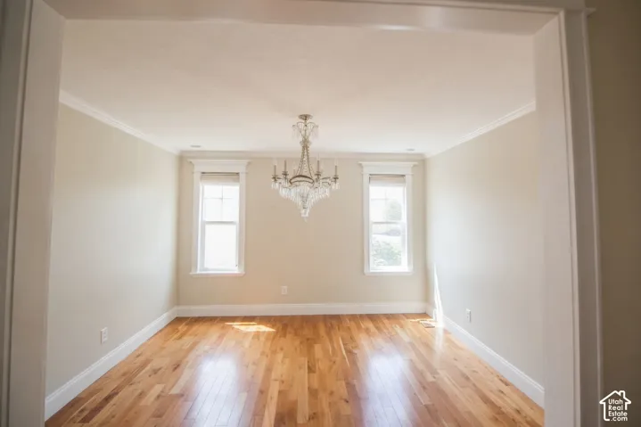 Spacious room featuring wood-finish flooring, a crystal chandelier, crown molding, and two windows with trim