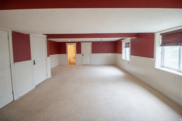 Spacious interior room featuring crimson walls over white wainscoting, light-toned carpet flooring, and multiple windows with included blinds