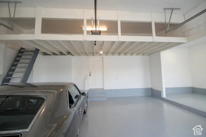Spacious garage featuring a finished gray floor, white walls, and a substantial overhead storage loft with a gray metal staircase