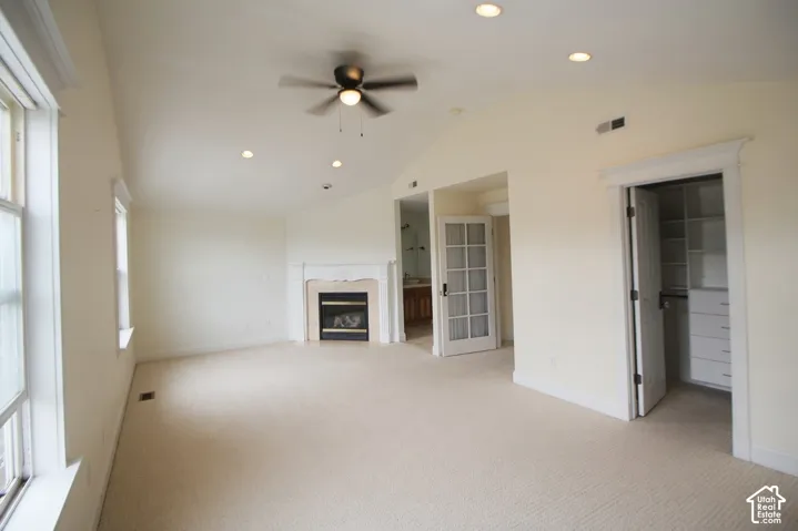 Spacious Master bedroom featuring vaulted ceilings, recessed lighting, a ceiling fan, a fireplace with a light-toned mantel, and multiple windows