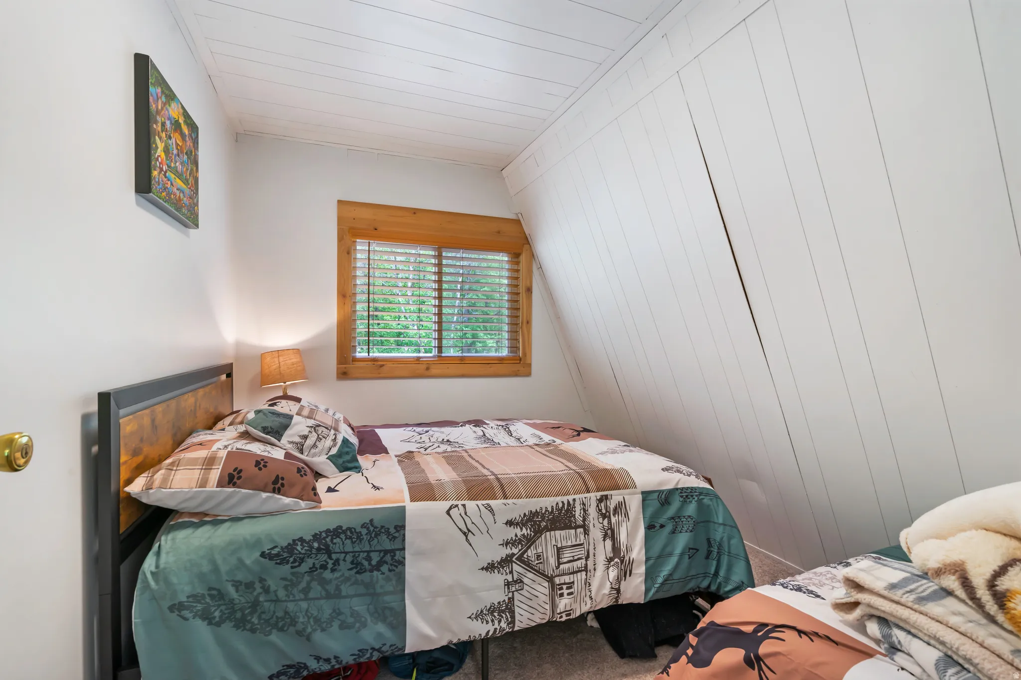 Attic room featuring a single window with wood trim, white shiplap ceiling, white wall paneling, and a light-toned carpet