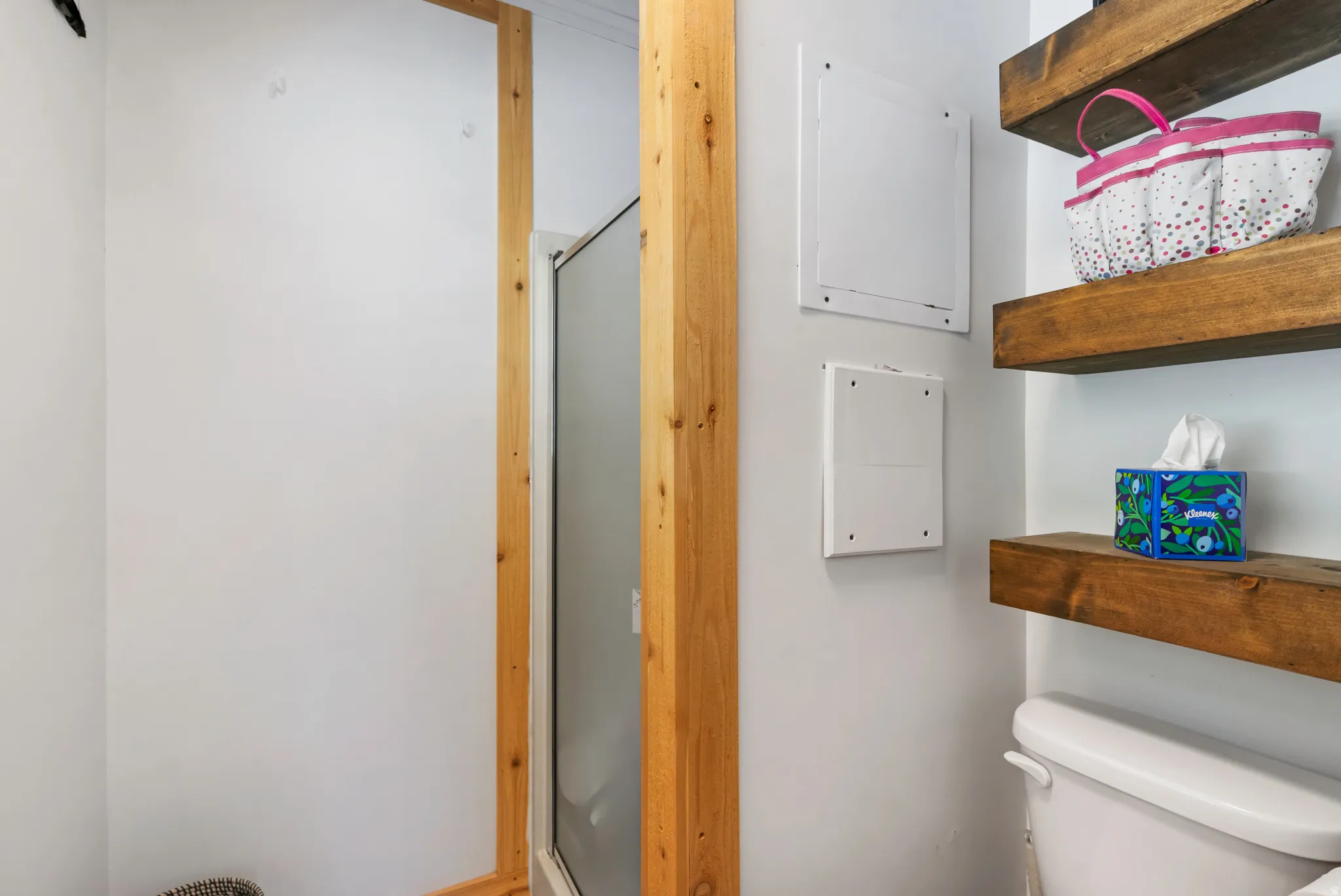 Corner shower enclosure with a clear glass panel and natural wood-tone framing, complemented by floating wood shelves