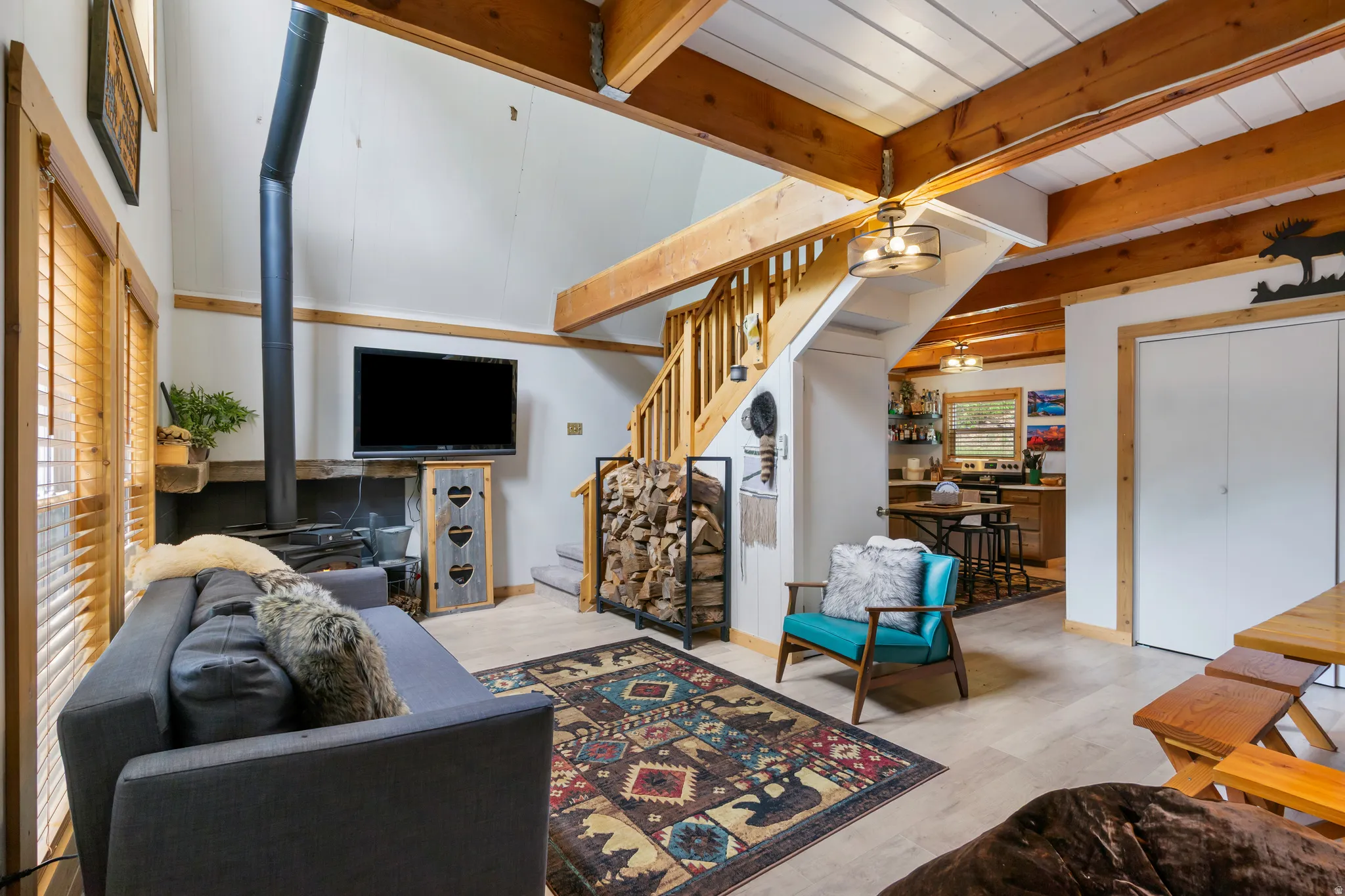 Vaulted ceiling with exposed wood beams, wood-finish flooring, wood stove, built-in wooden shelving, and a wooden staircase with railing