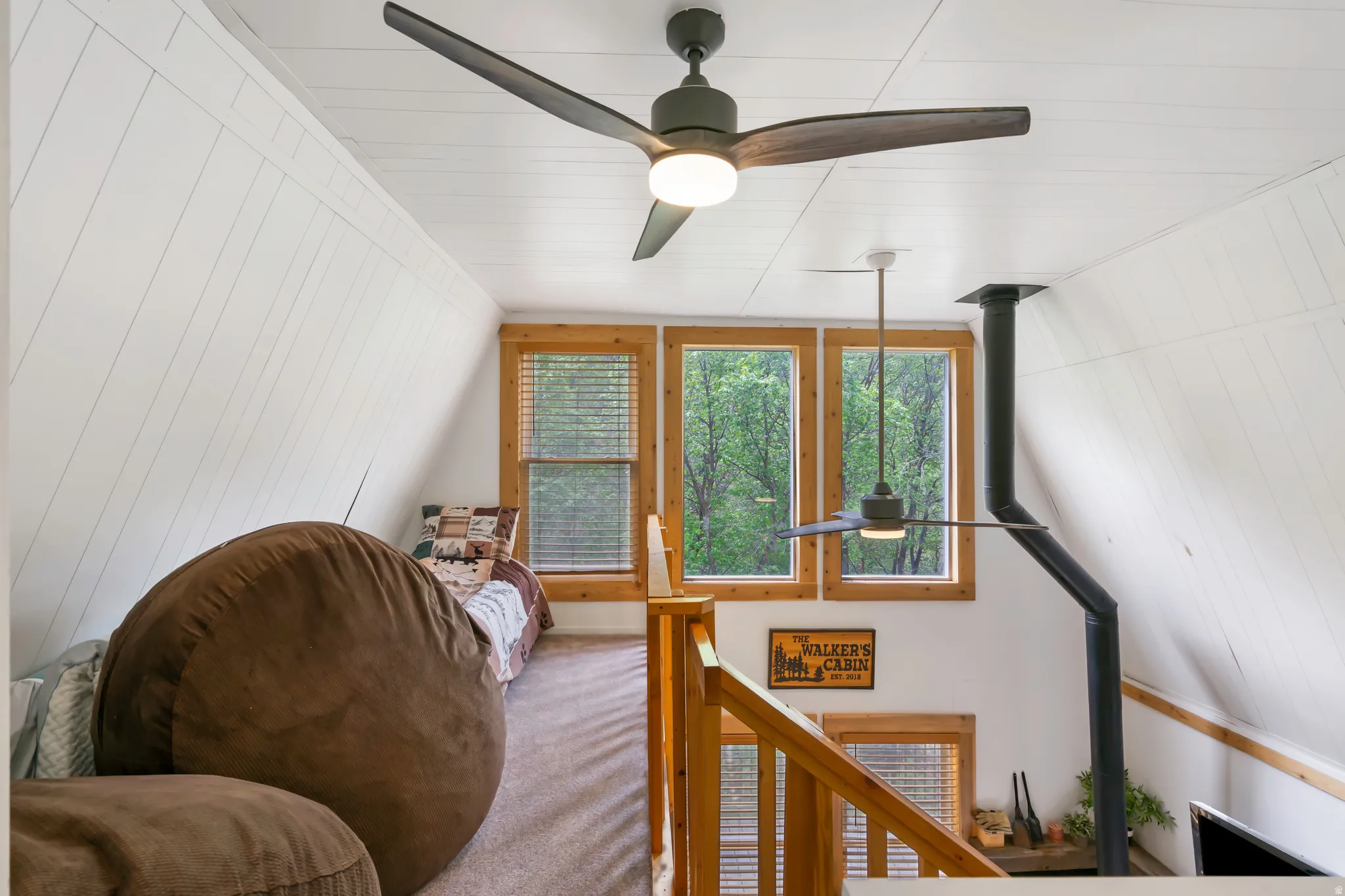 A-frame interior featuring white shiplap walls, wood-framed windows, and ceiling fans with integrated lighting
