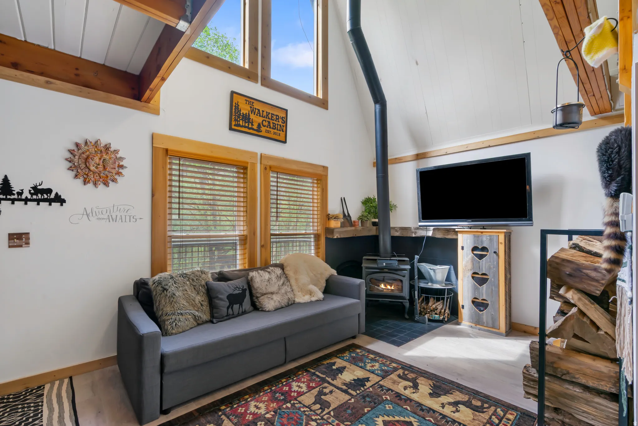 Living area featuring a wood-burning stove with black hearth tiling, vaulted ceilings with wood beams, and a light wood-finish floor