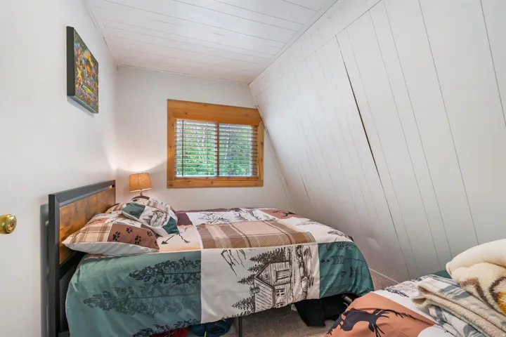 Attic room featuring a single window with wood trim, white shiplap ceiling, white wall paneling, and a light-toned carpet