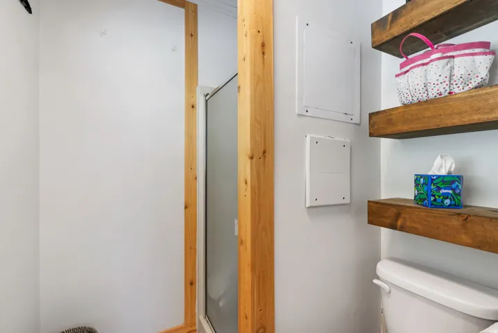 Corner shower enclosure with a clear glass panel and natural wood-tone framing, complemented by floating wood shelves
