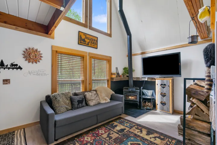 Living area featuring a wood-burning stove with black hearth tiling, vaulted ceilings with wood beams, and a light wood-finish floor