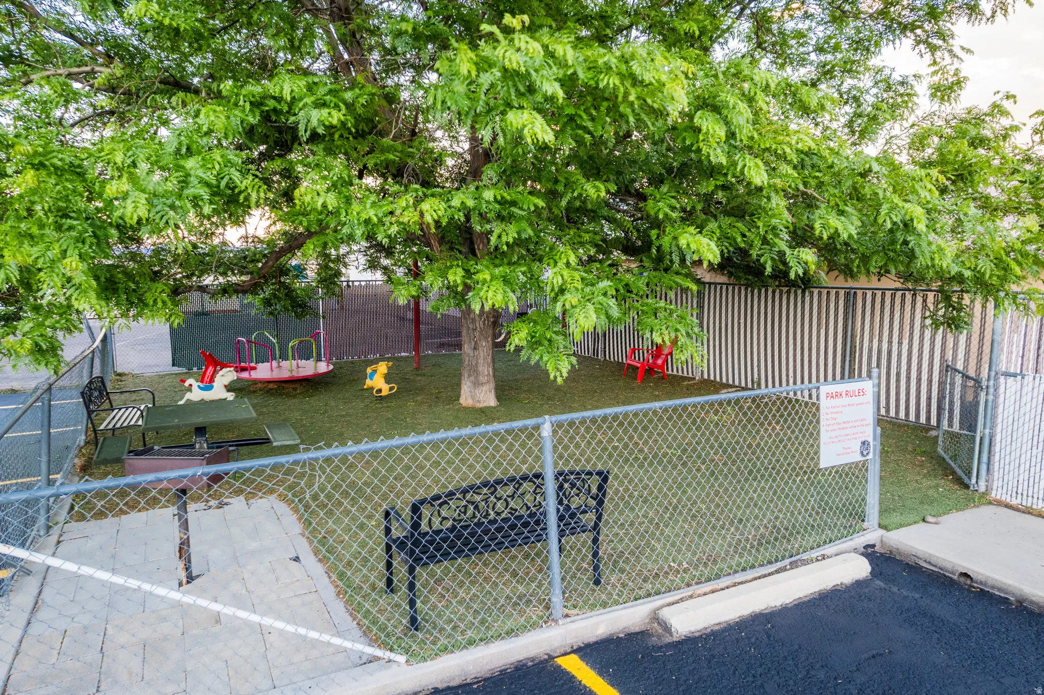 Fenced outdoor area featuring an artificial turf surface and mature shade tree