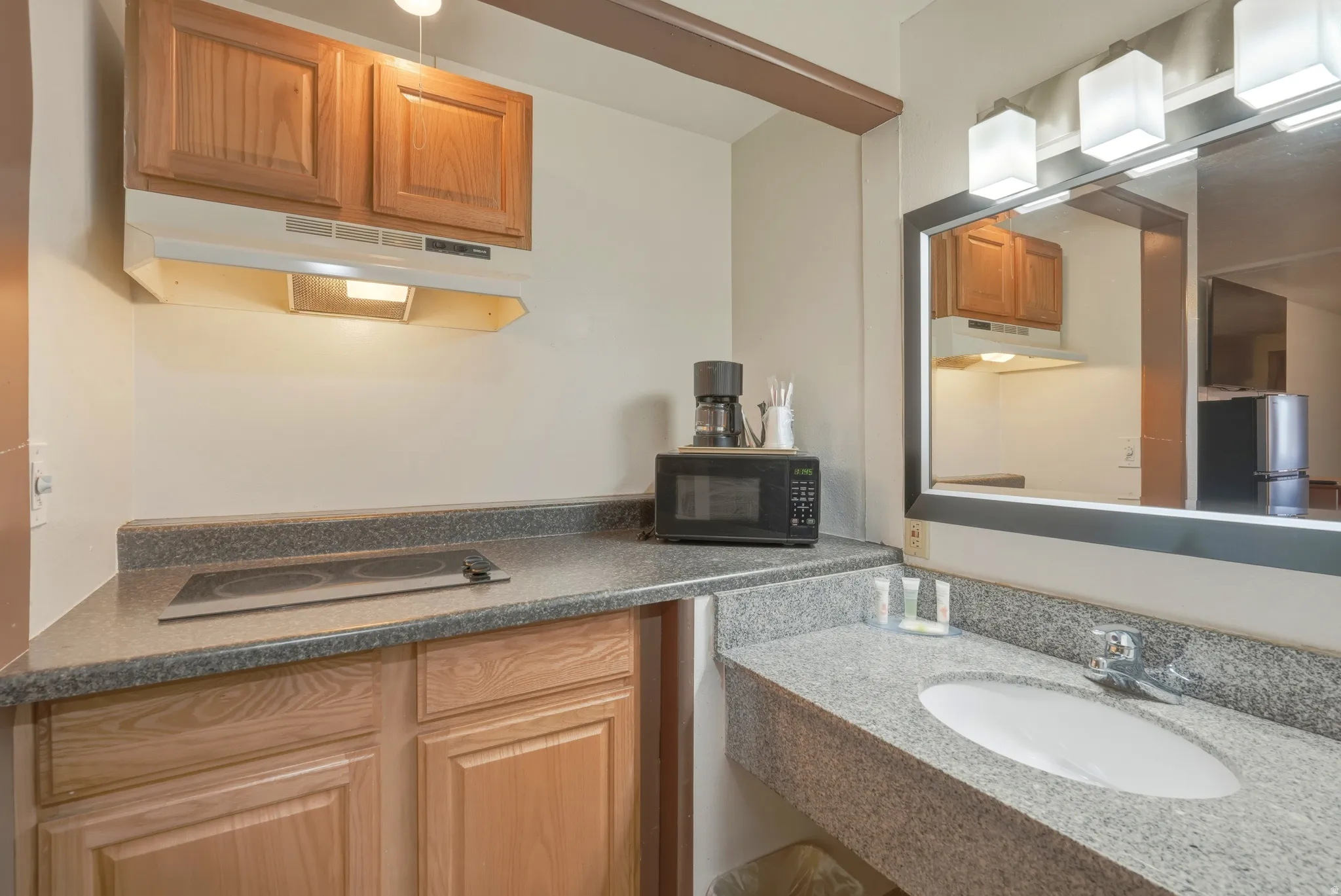 Compact kitchenette featuring a built-in electric cooktop, wood cabinetry, and a range hood