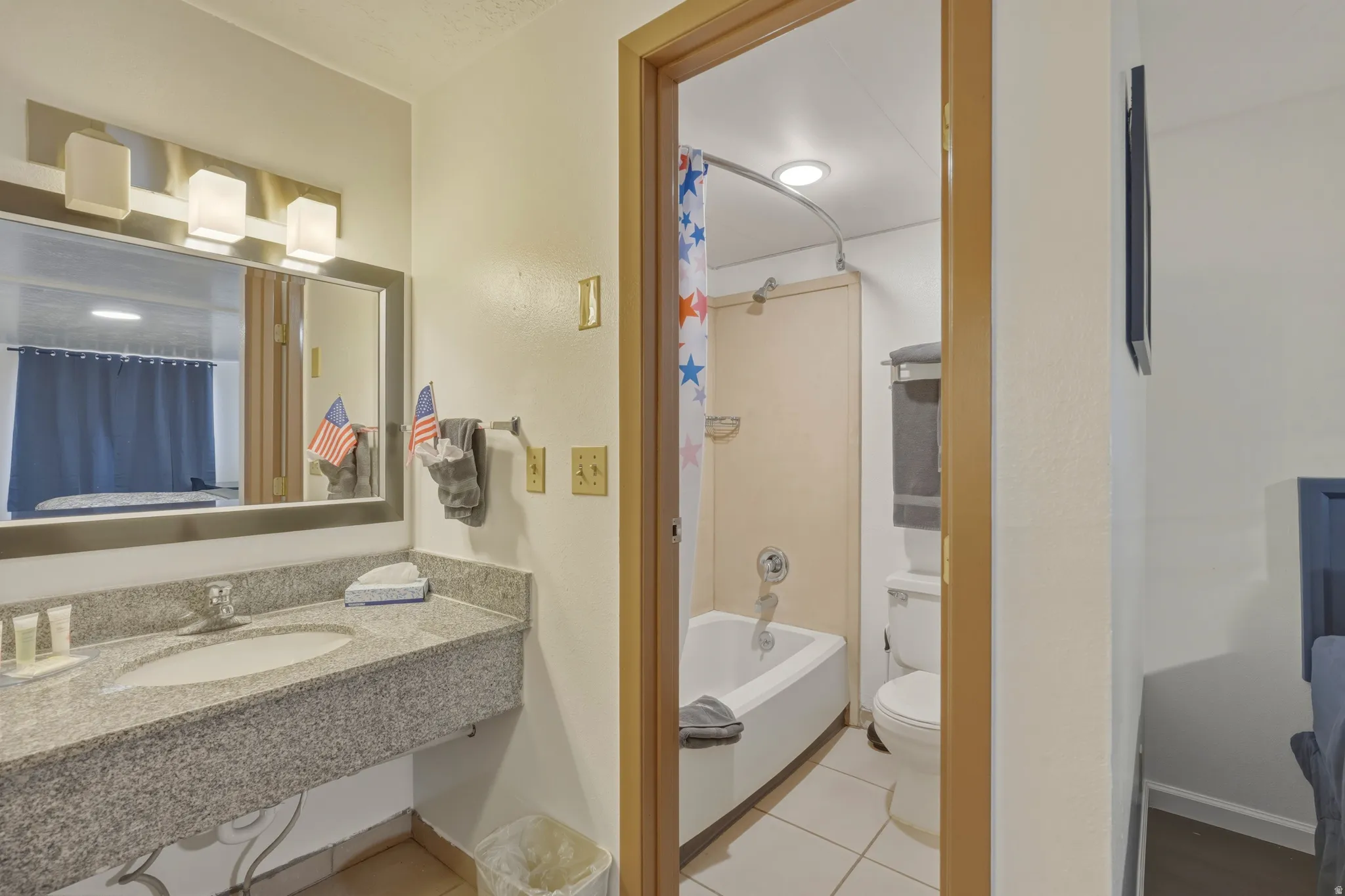 Bathroom featuring a granite-look vanity with an integrated sink, a large mirror, and a wall-mounted light fixture
