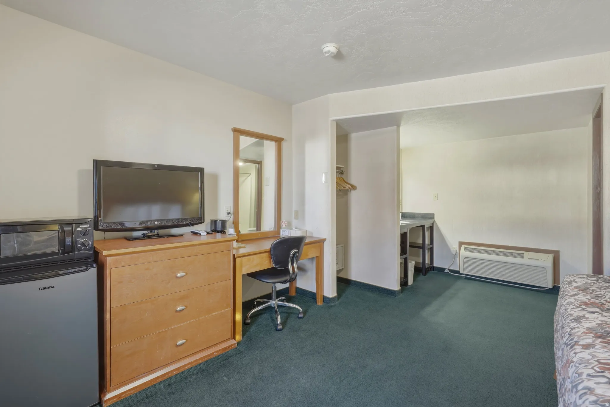 Carpeted interior space featuring a built-in air conditioning unit, a dedicated vanity with mirror, and a wood-finish dresser