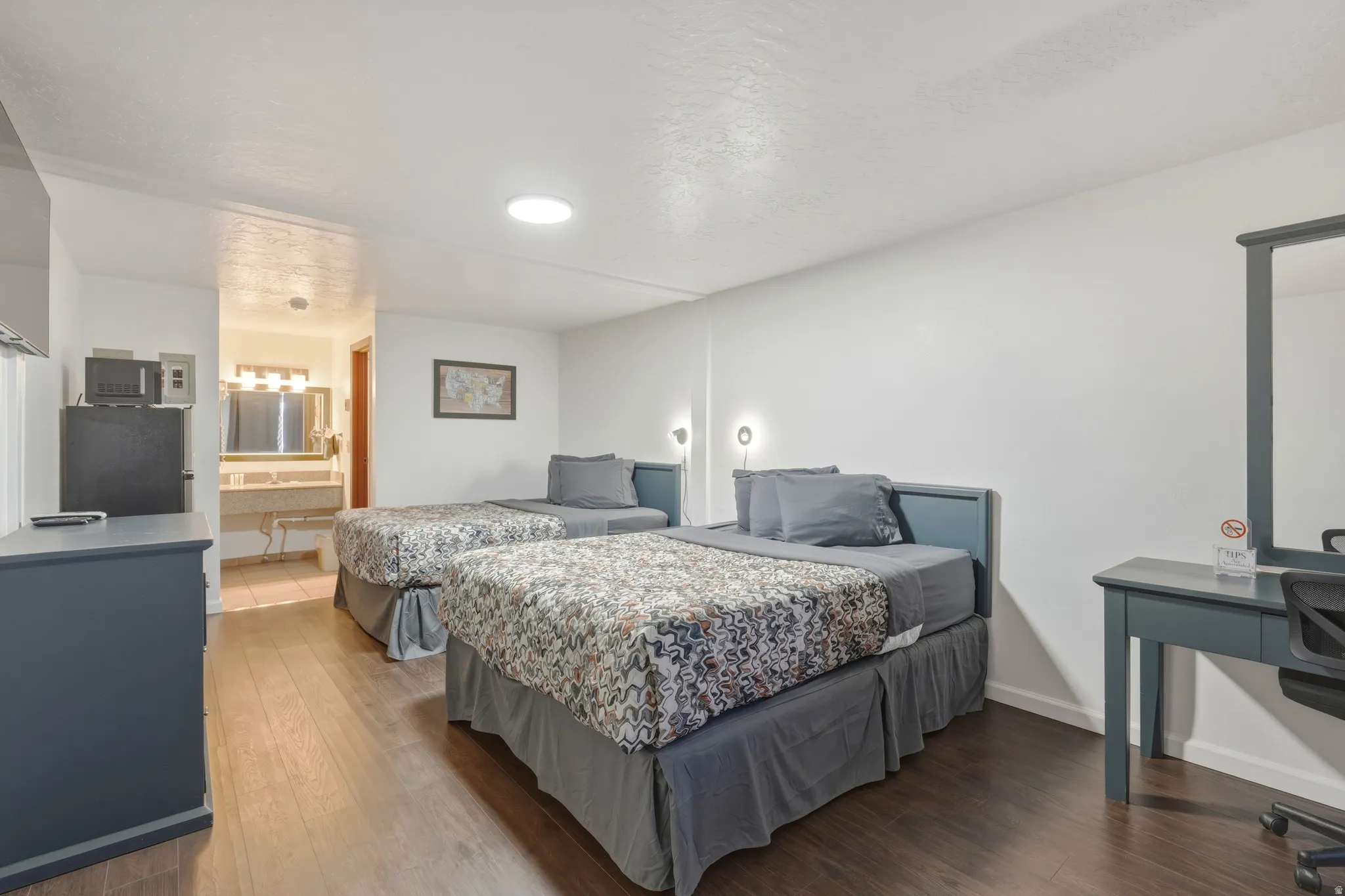 Spacious room featuring two beds with coordinated headboards, wood-finish flooring, and a dedicated desk area