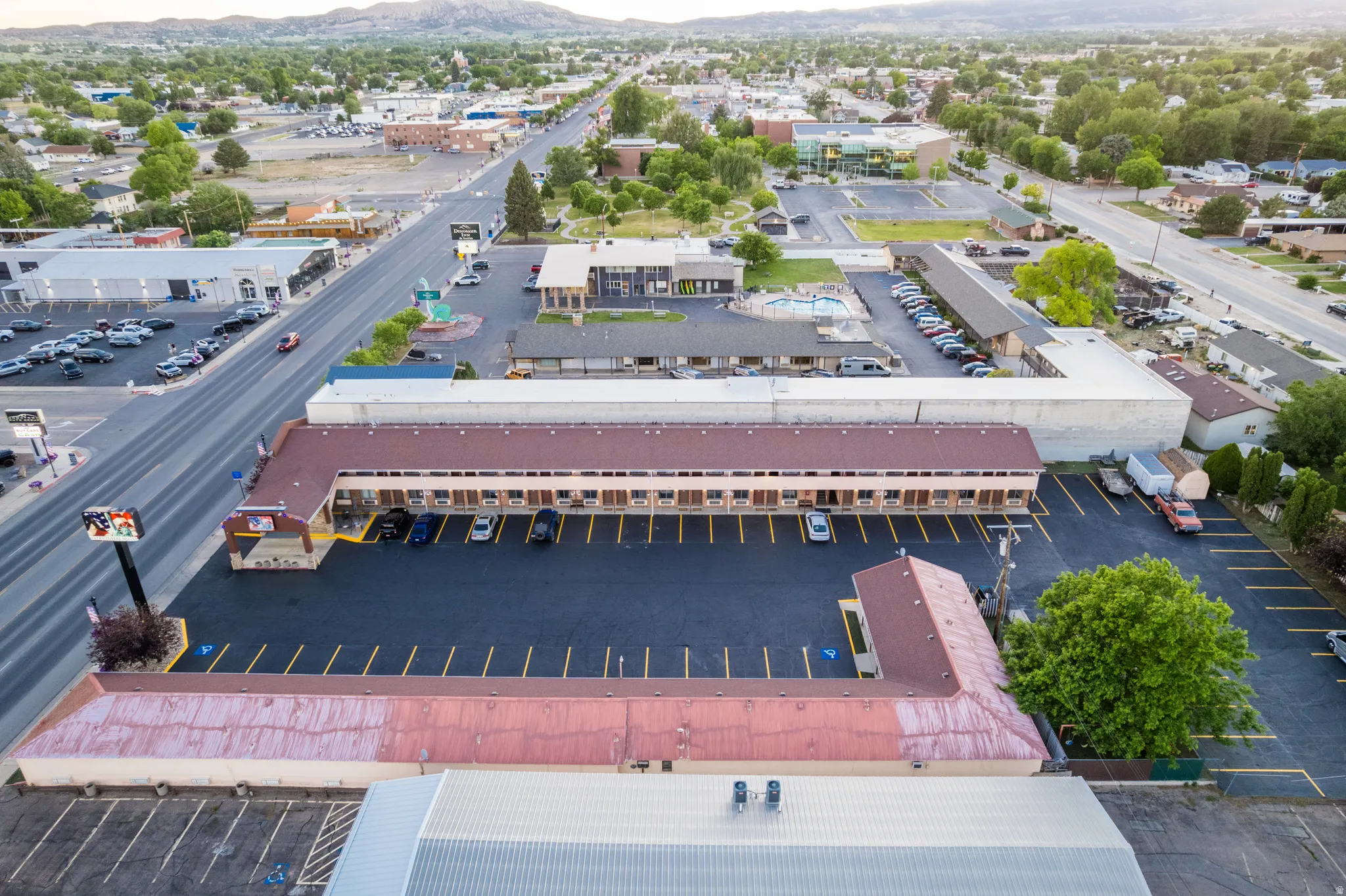 Aerial perspective showcasing a commercial property with extensive paved parking, multiple single-story structures with reddish-brown roofs, and a prominent roadside sign