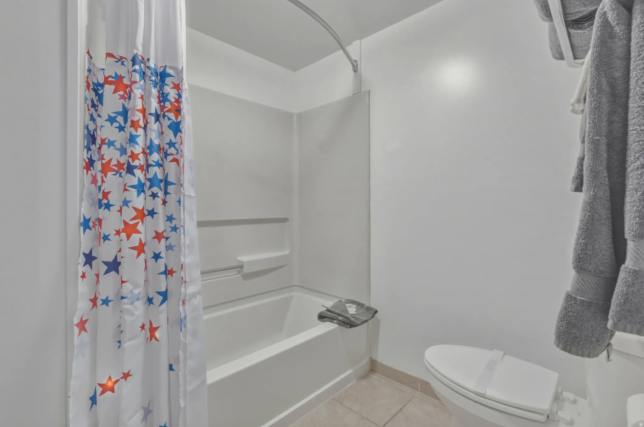 Bathroom featuring a white tub and shower combination with a single-piece surround, a white toilet, and neutral tile flooring