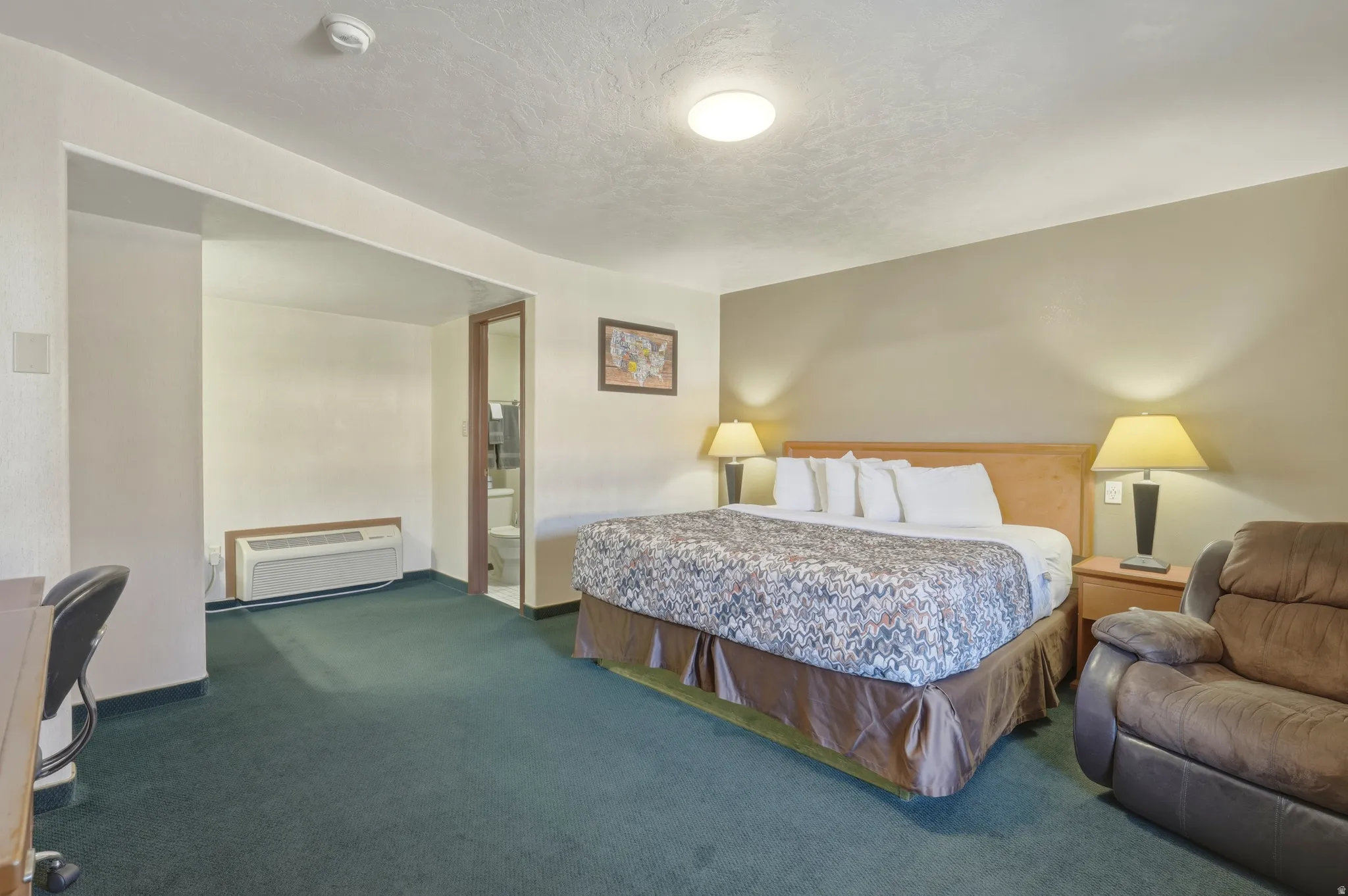 Carpeted room with a wooden headboard, two bedside tables with lamps, and a wall-mounted air conditioning unit