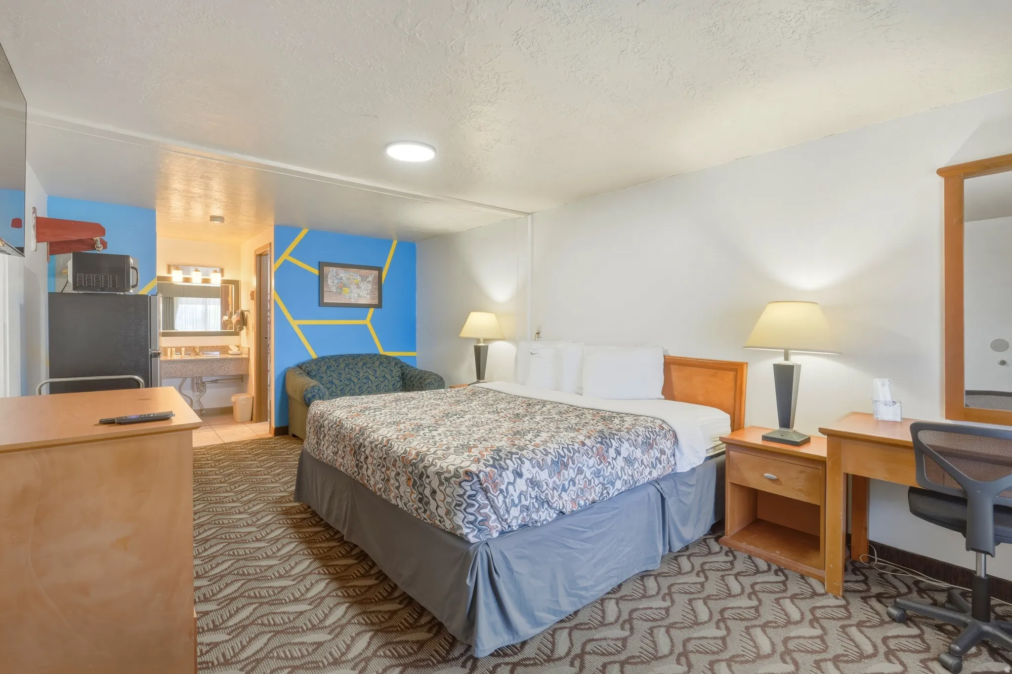 Carpeted room featuring a bed with a wooden headboard, a wooden nightstand, and a desk with an office chair