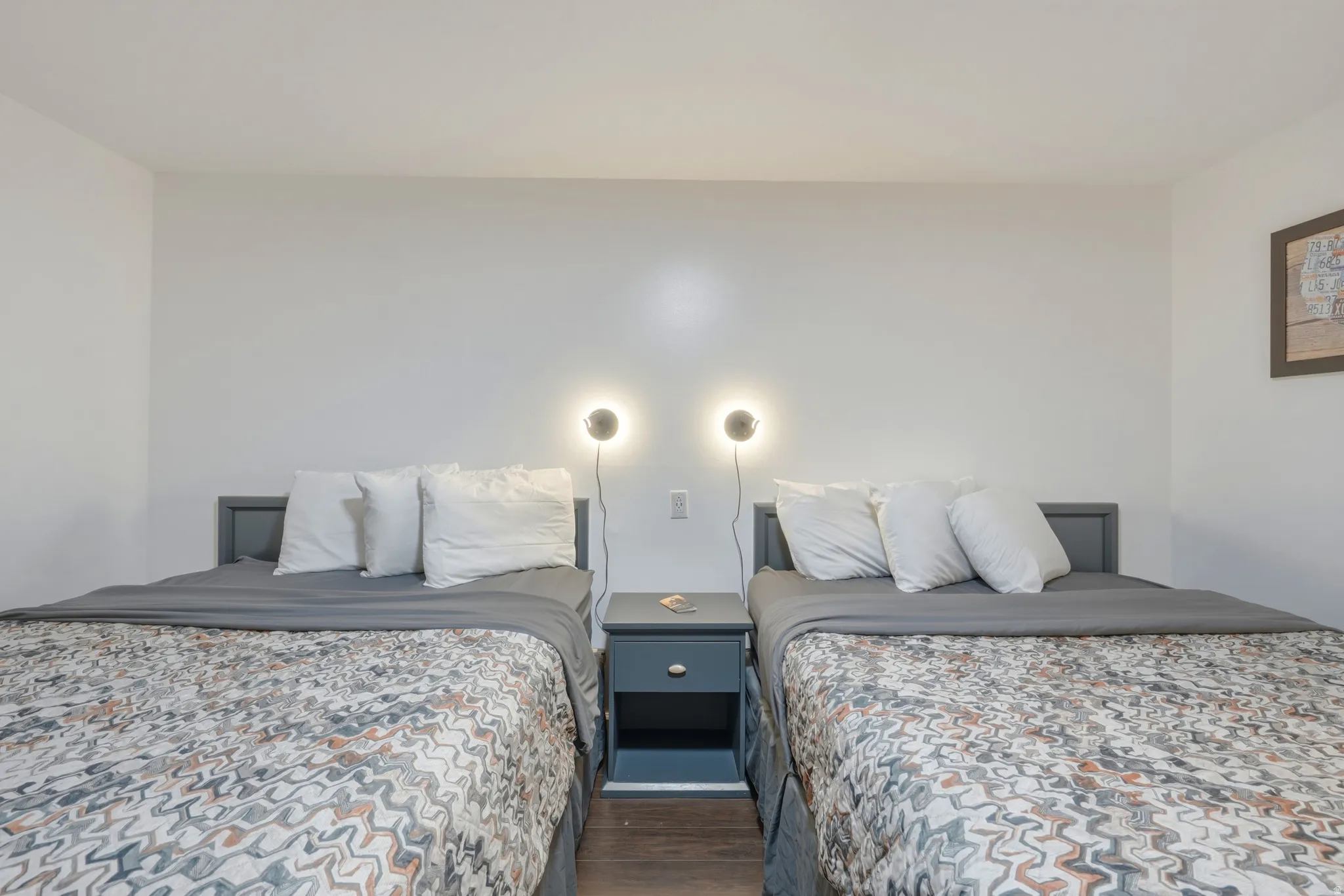 Twin beds with grey wood frames, central nightstand, modern wall sconces, and dark wood-finish flooring