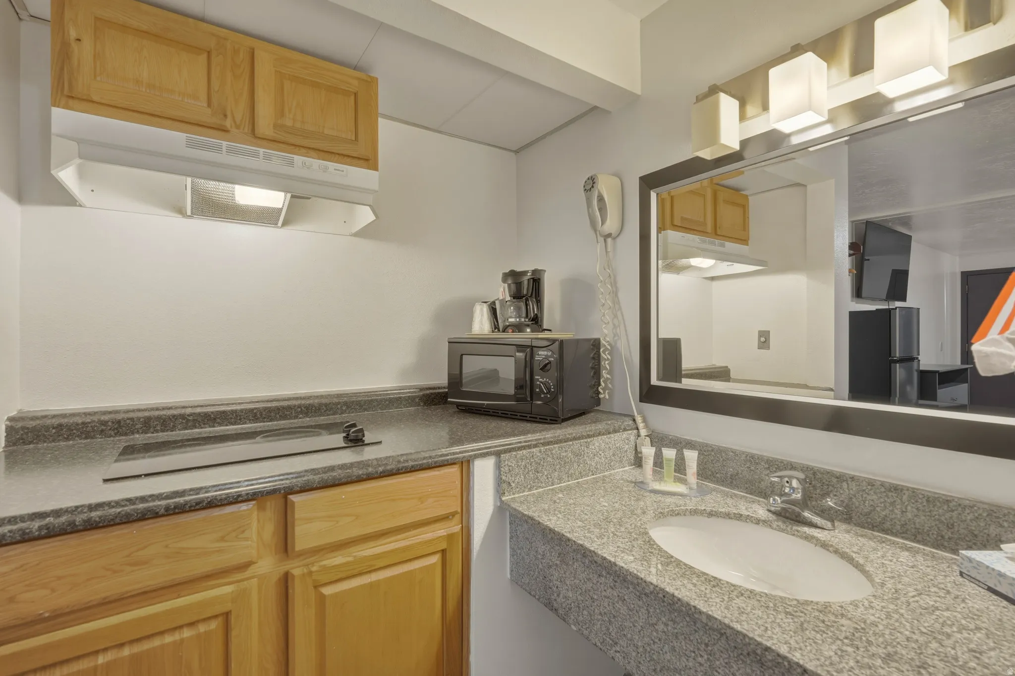 Compact kitchen and vanity area featuring wood cabinetry, a built-in cooktop, and a countertop microwave