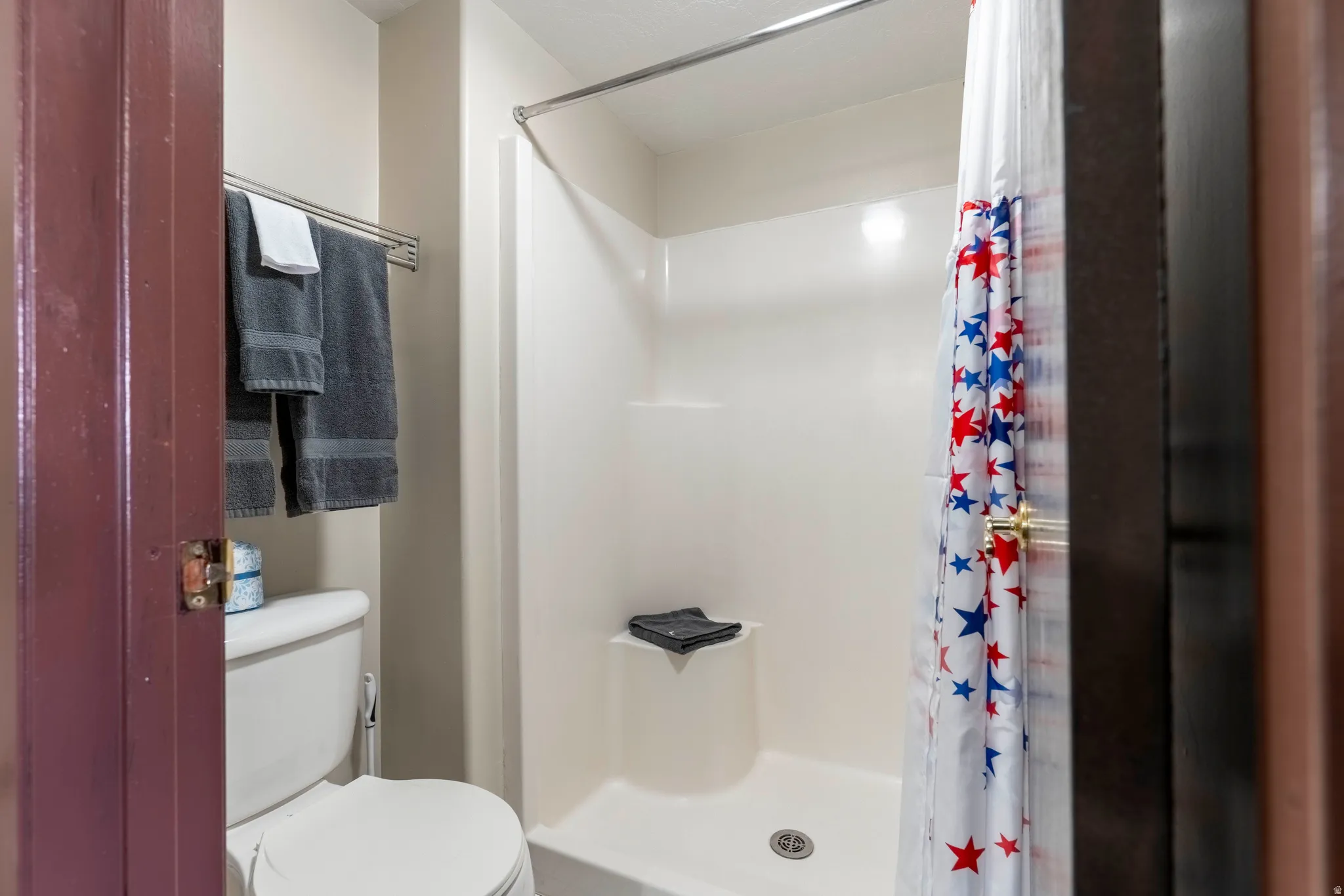 White shower enclosure with a built-in seat, chrome shower rod, and a white toilet