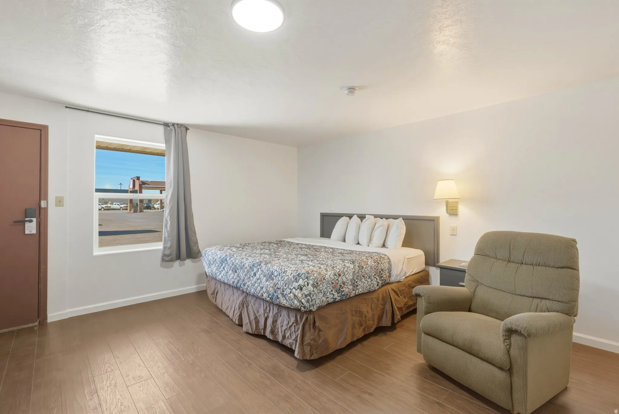 Bedroom with wood-finish flooring, a single window with curtain rod, and a wall-mounted light fixture