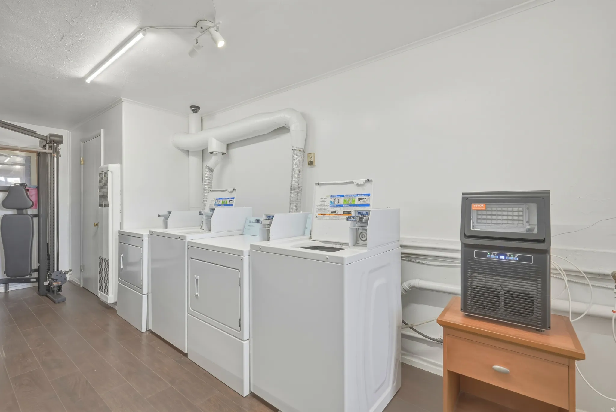 Dedicated laundry area featuring multiple white appliances, overhead track lighting, wood-finish flooring, and white painted walls