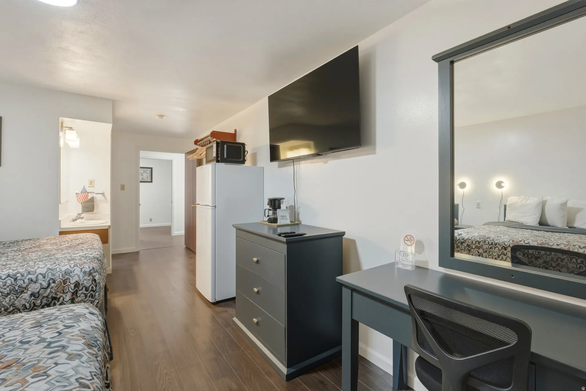 Interior room featuring dark wood-finish flooring, a wall-mounted television, a full-size refrigerator, a built-in vanity with a mirror, and recessed lighting