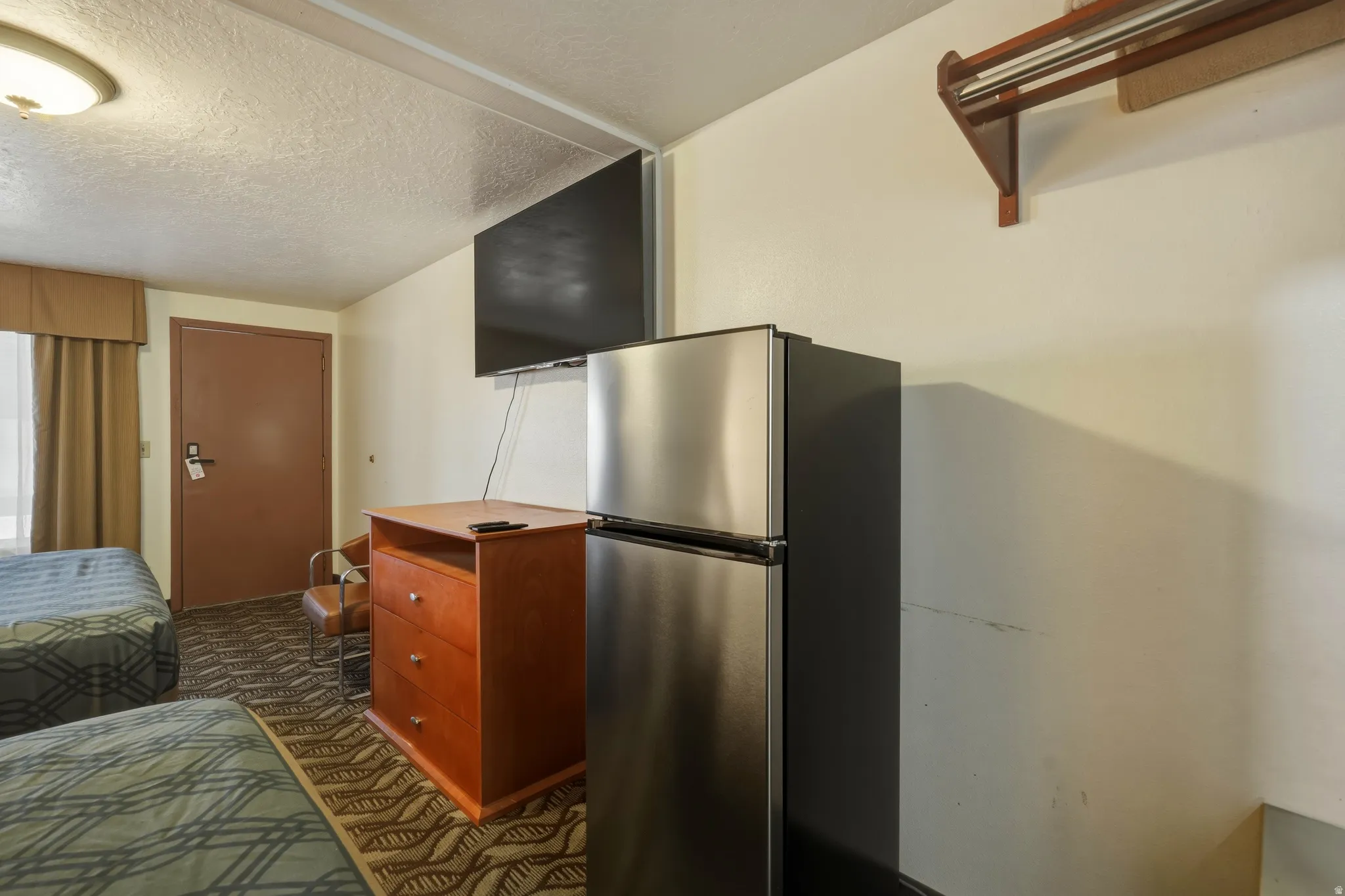 Compact room featuring twin beds, wall-mounted television, and a stainless steel refrigerator
