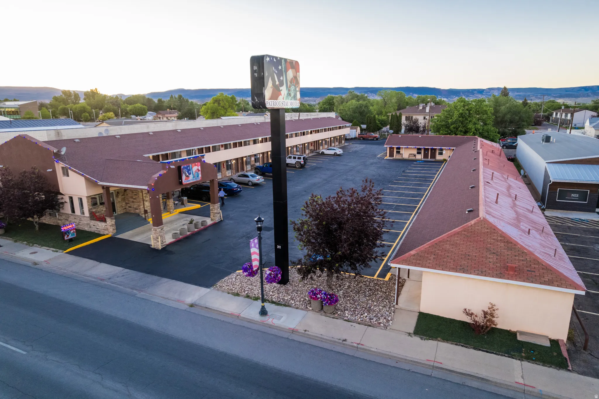 Expansive property featuring multiple buildings with red-hued shingle roofing, extensive paved parking areas, and a prominent roadside sign structure