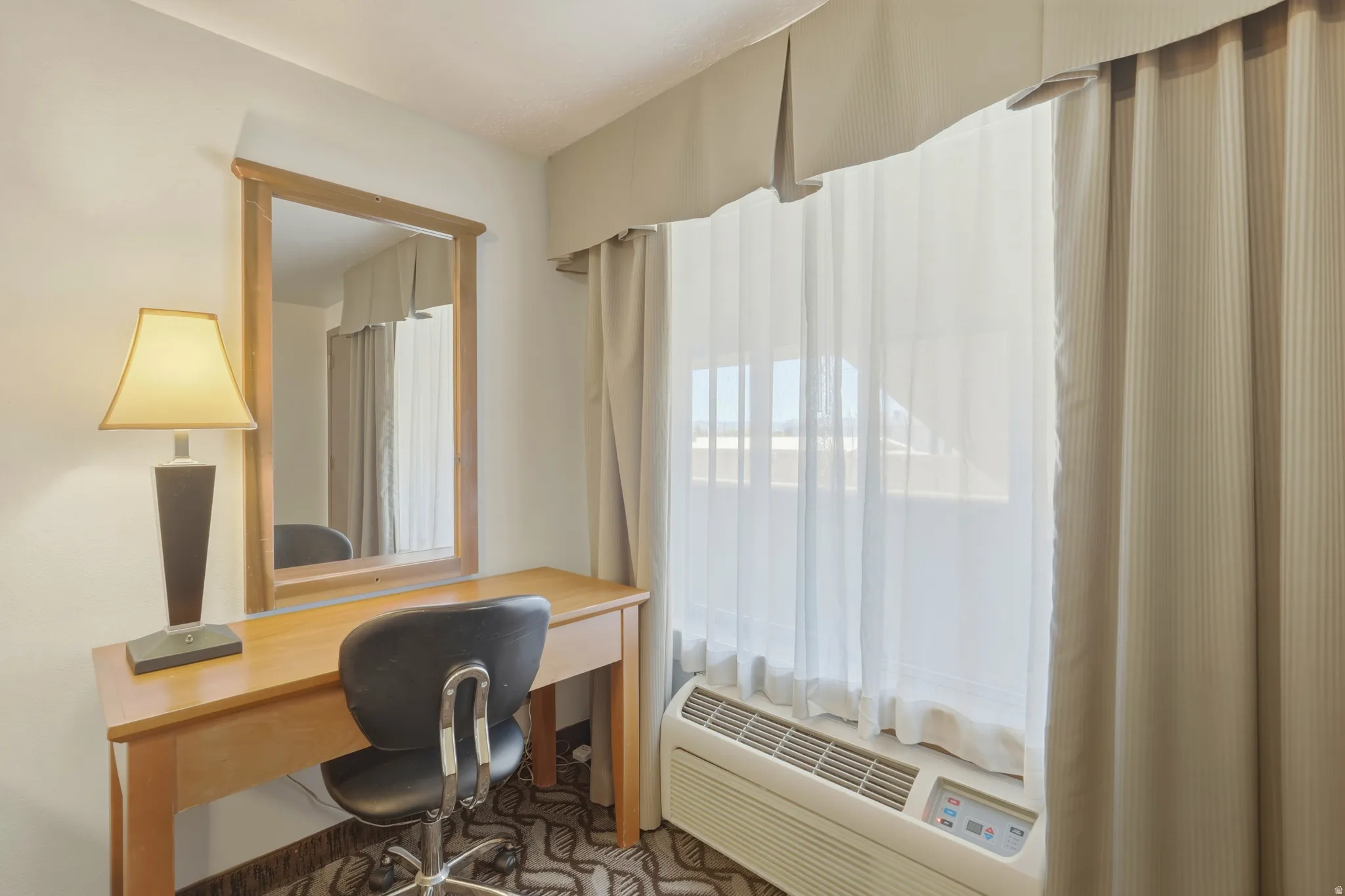 Dedicated desk area featuring a light wood-finish desk with a matching framed wall mirror, and neutral-toned window treatments with sheer and blackout options