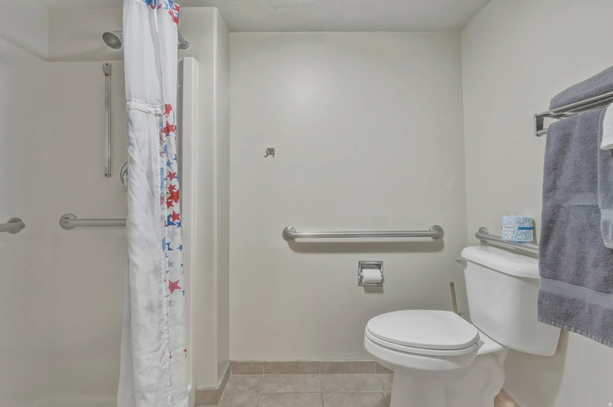 Bathroom featuring a shower stall with built-in grab bars, a standard toilet, and tiled flooring