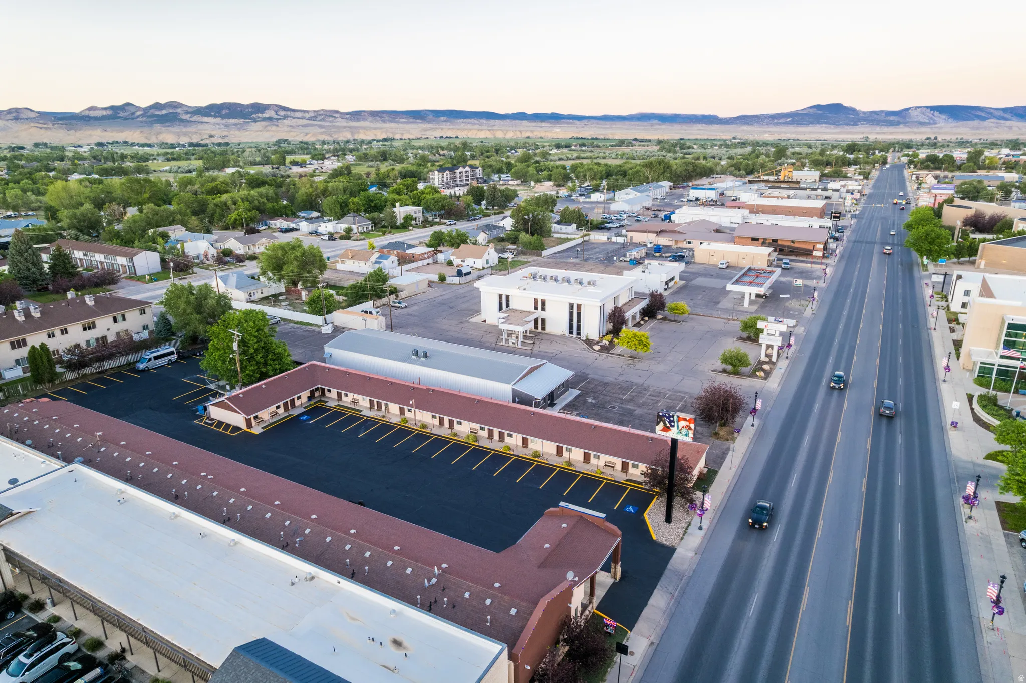 Extensive commercial property featuring a large asphalt parking lot with striped spaces, a multi-unit building with a red shingle roof, and a prominent commercial sign