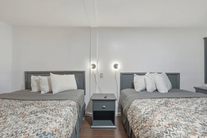 Bedroom featuring two beds with dark gray headboards, dark wood-finish flooring, white walls, and wall-mounted sconce lighting
