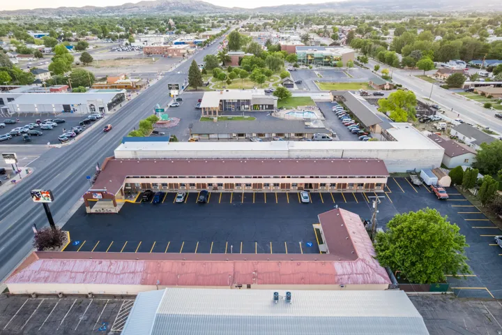 Aerial perspective showcasing a commercial property with extensive paved parking, multiple single-story structures with reddish-brown roofs, and a prominent roadside sign