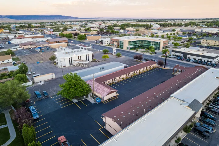 Expansive commercial property featuring multiple structures, a large paved parking area with marked spaces, and established trees