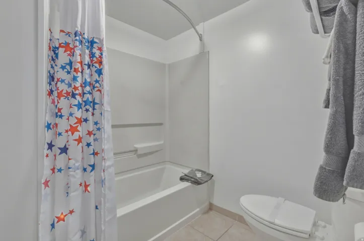 Bathroom featuring a white tub and shower combination with a single-piece surround, a white toilet, and neutral tile flooring