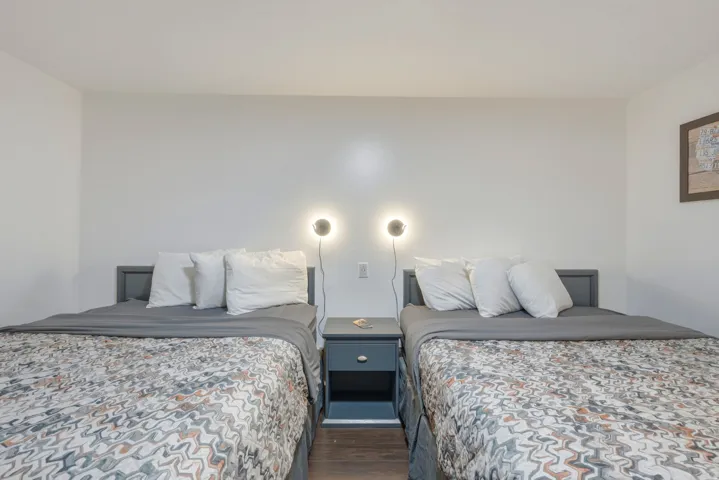Twin beds with grey wood frames, central nightstand, modern wall sconces, and dark wood-finish flooring