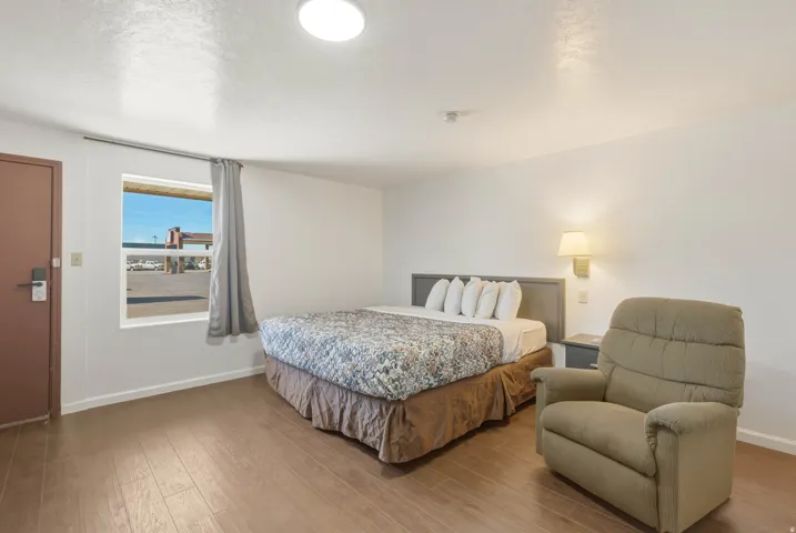 Bedroom with wood-finish flooring, a single window with curtain rod, and a wall-mounted light fixture