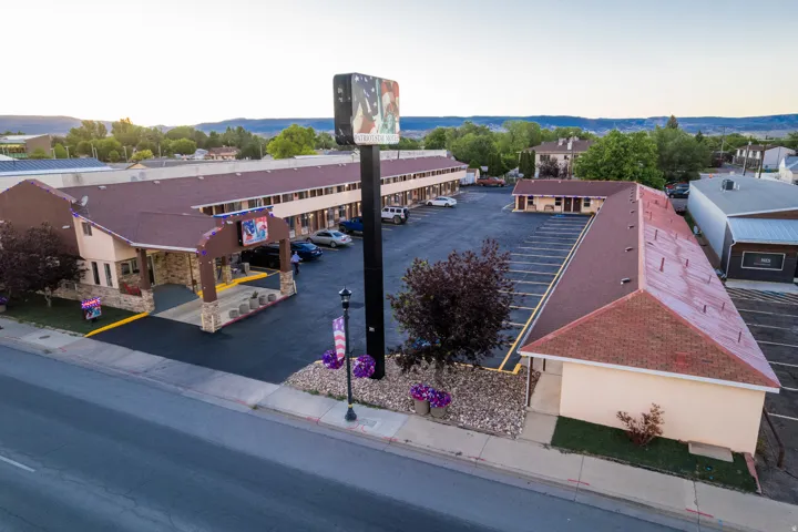 Expansive property featuring multiple buildings with red-hued shingle roofing, extensive paved parking areas, and a prominent roadside sign structure