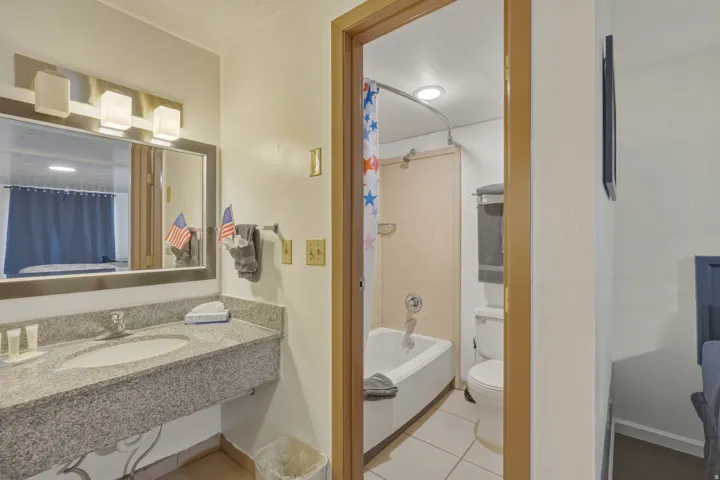 Bathroom featuring a granite-look vanity with an integrated sink, a large mirror, and a wall-mounted light fixture