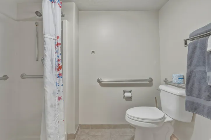 Bathroom featuring a shower stall with built-in grab bars, a standard toilet, and tiled flooring