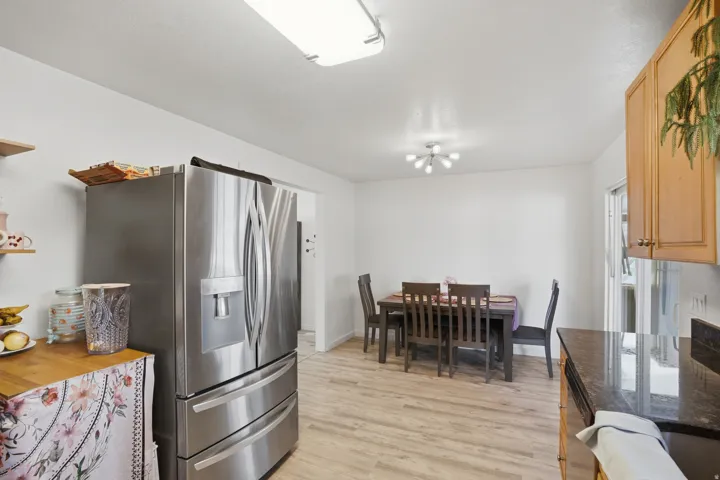 Spacious kitchen and dining area featuring wood-finish flooring, a stainless steel refrigerator, granite-style countertops, and light wood cabinetry