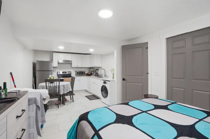 Open-concept living space featuring a compact kitchen with white cabinetry and stainless steel appliances, durable tile flooring, and contrasting gray interior doors